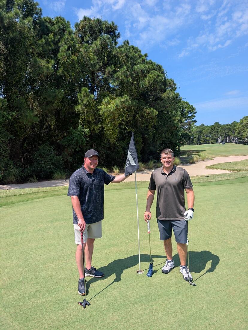 Two veterans posing with the flag on the green at Raven Golf Club