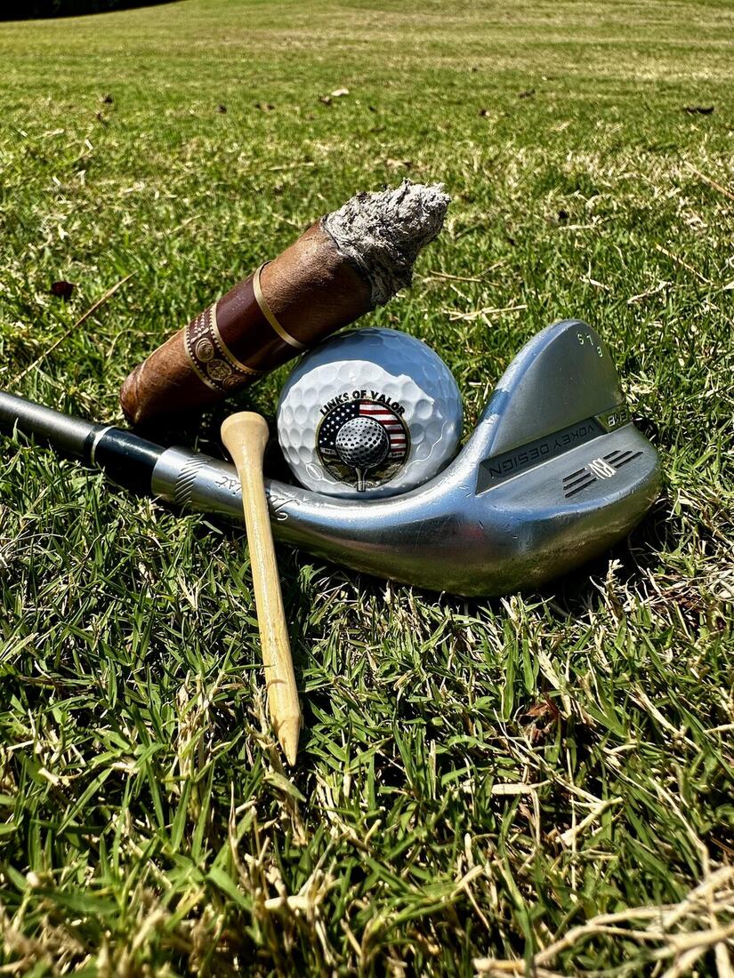 A Links of Valor golf ball resting in a wedge beside a cigar